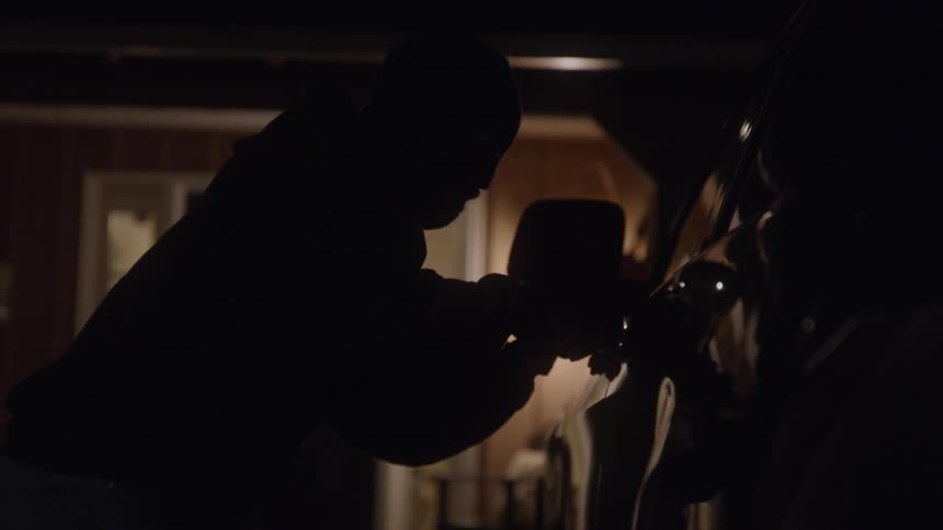 The video shows a person in a dark setting getting out of a vehicle in a driveway and walking toward a house with a lit porch the scene is dark with only the light from the house and a reflection on the car providing illumination