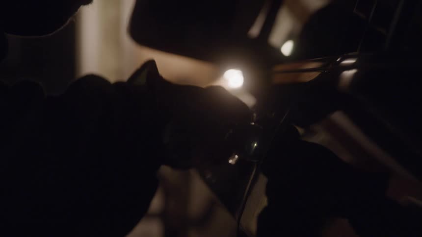 A low close and dark view shows a person wearing black gloves opening the door of a vehicle