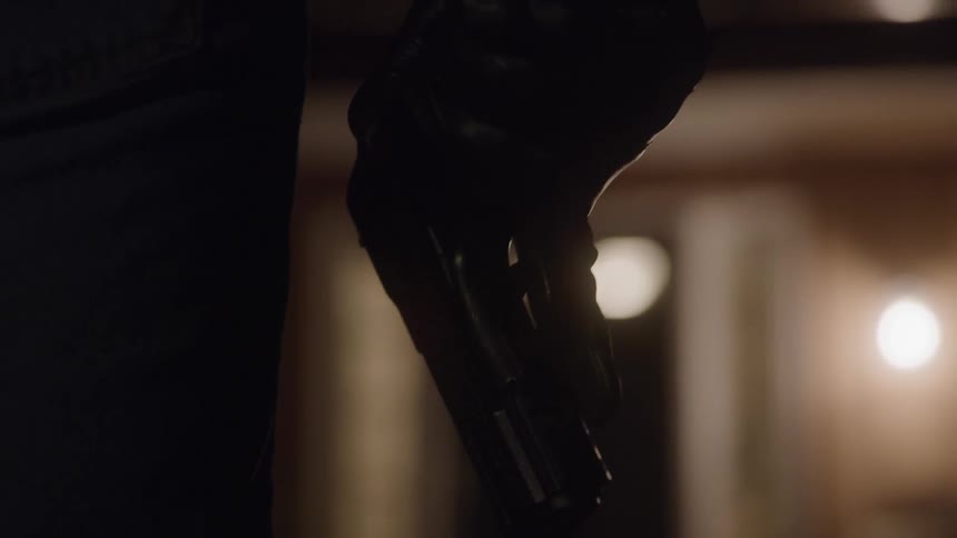 A gloved hand holding a gun pointed to the ground
