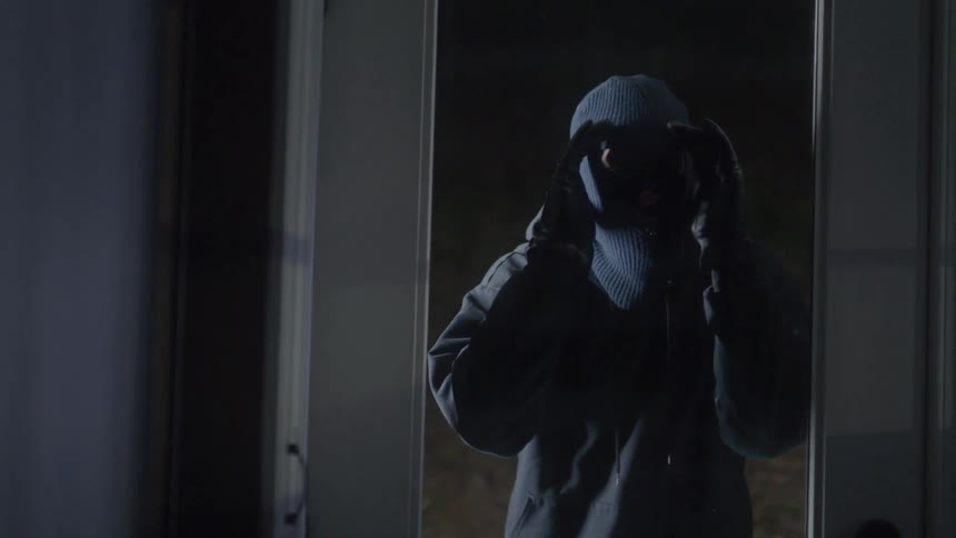 Man wearing a ski mask looks in through a glass door