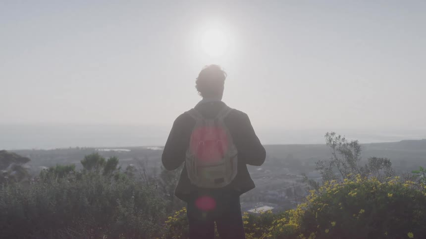 A backpacker stands on top of a hill and contemplates the view of the town below