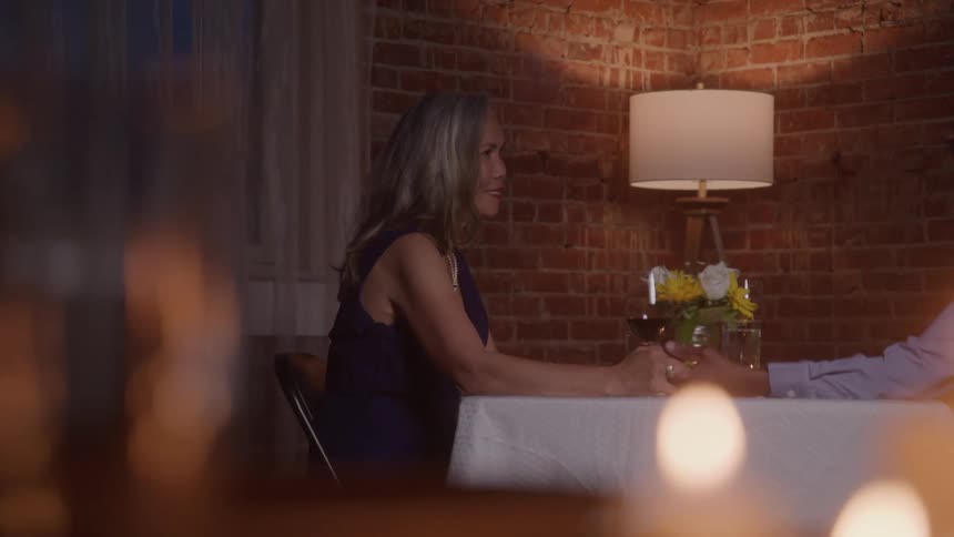 Mature couple sitting at a table lit by lamp and candles holding hands