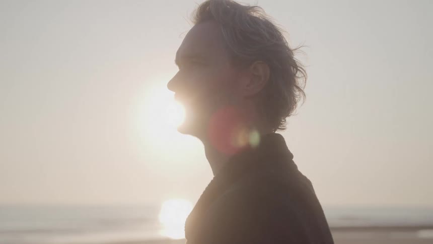 A pensive man stands on a beach and gazes at the sea