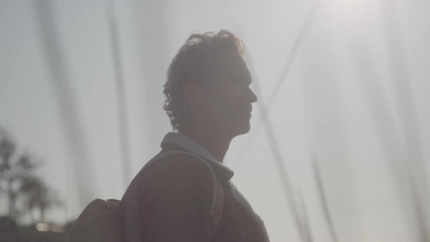 A silhouette of a person seen from the side looks out at a hazy sunlit scene the light is so bright it creates a strong lens flare effect in the camera