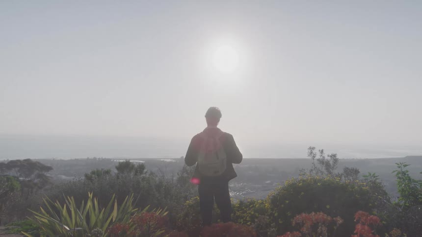 A backpacker standing at the top of a hill contemplating the view below