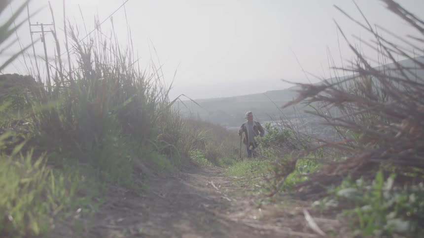 Man hiking along a path on a hill on a foggy day uses a pair of walking poles