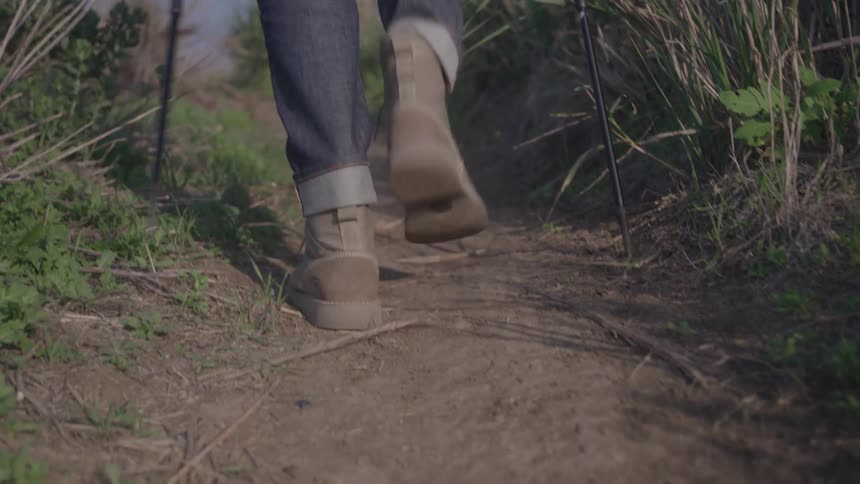 Two individuals are hiking on a dirt path one person is wearing lightcolored boots and jeans and is using a hiking pole