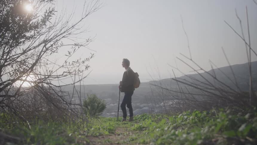 The man hiking stops to look over the mountain peak