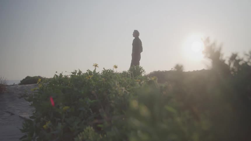 A person stands alone on a rocky path at sunset