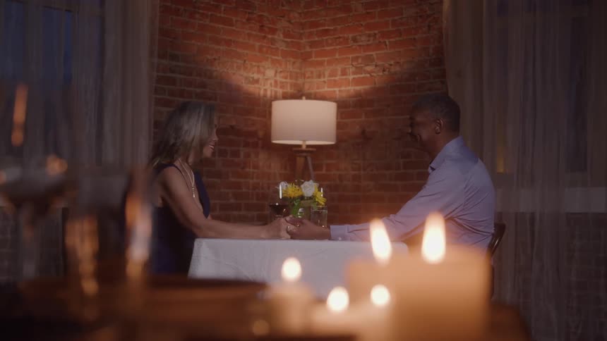 Mature couple smiling while holding hands at a candlelit dinner
