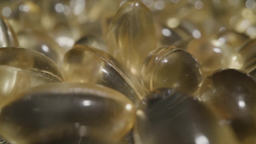 A closeup panning shot moves across a large pile of golden translucent softgel capsules that are bunched together