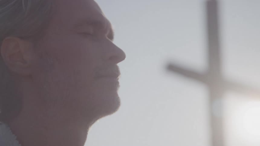 A profile shot of a man with graying hair shows him looking up with his eyes closed he appears to be soaking in the bright sunlight which is shining from behind and casting a soft glow