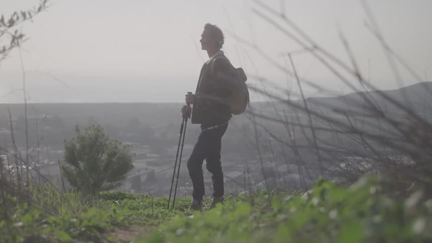 A backpacker standing at the top of a hill above a town contemplating the view