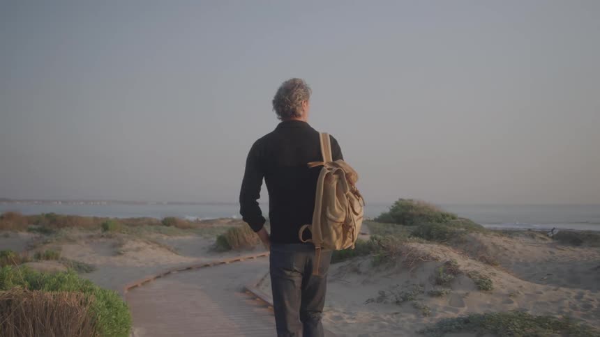 Man walking on a path on the coast with a backpack over his shoulder