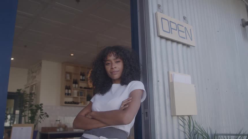 Woman wearing an apron with arms crossed in front of a shop with an open sign