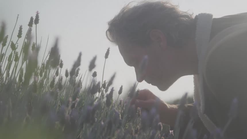 The man leans forward to smell the flowers