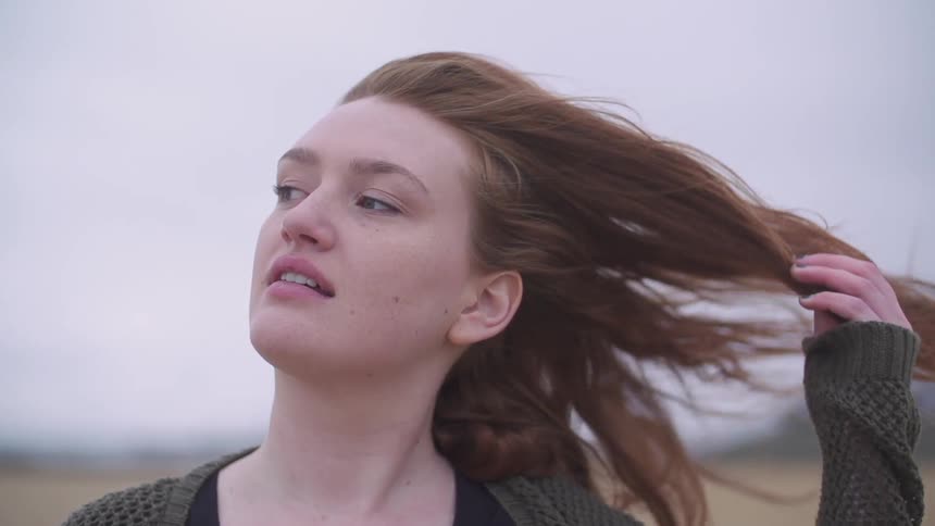 A woman puts her hand through her hair on a cloudy day