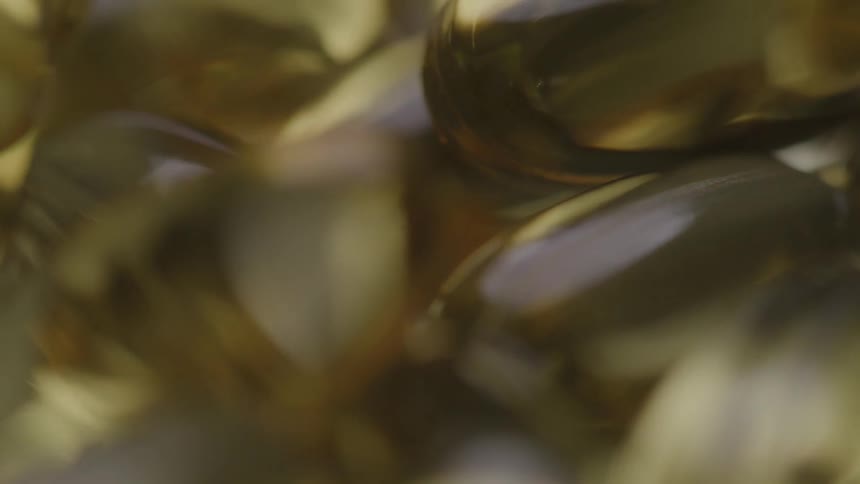 A rotating macro shot shows a pile of shiny goldencolored soft gel vitamin capsules shifting and moving
