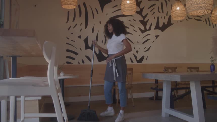 A young black woman sweeps the restaurant floor during daytime