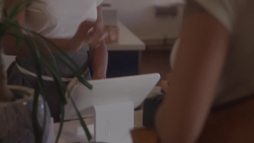 A client makes a payment at a coffee shop and the young woman at the counter talks to her then they both laugh