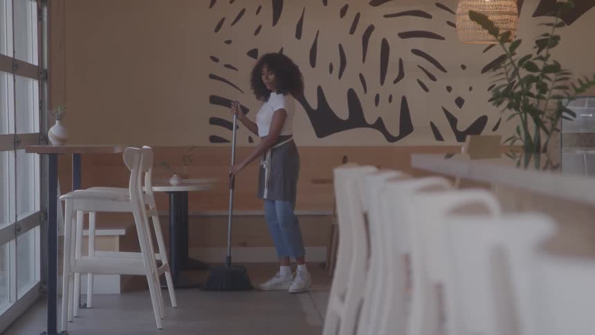 The woman is sweeping in the corner of the restaurant