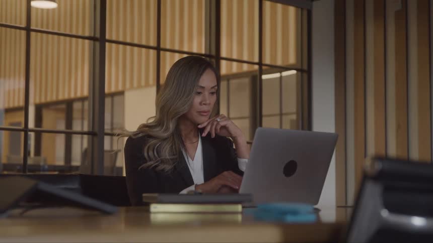 A focused woman at a desk in an office working on a laptop