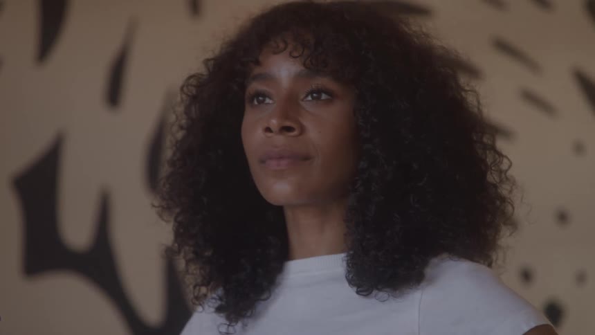 A closeup shot of a woman with curly hair looking offcamera with a contemplative expression