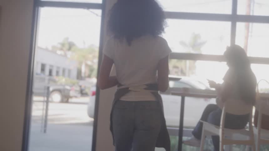 A shot of a waitress with curly hair serving a customer at a cafe highlighting the brief and friendly interaction between them
