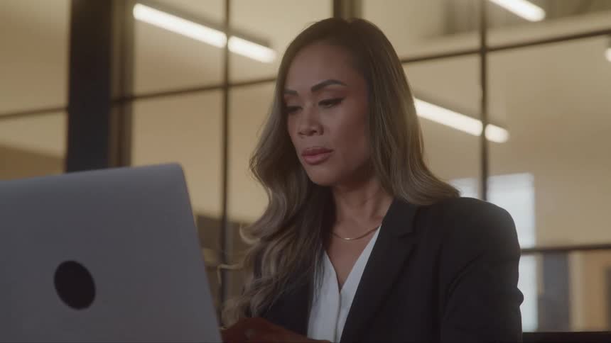 A woman is sitting in an office typing on a laptop