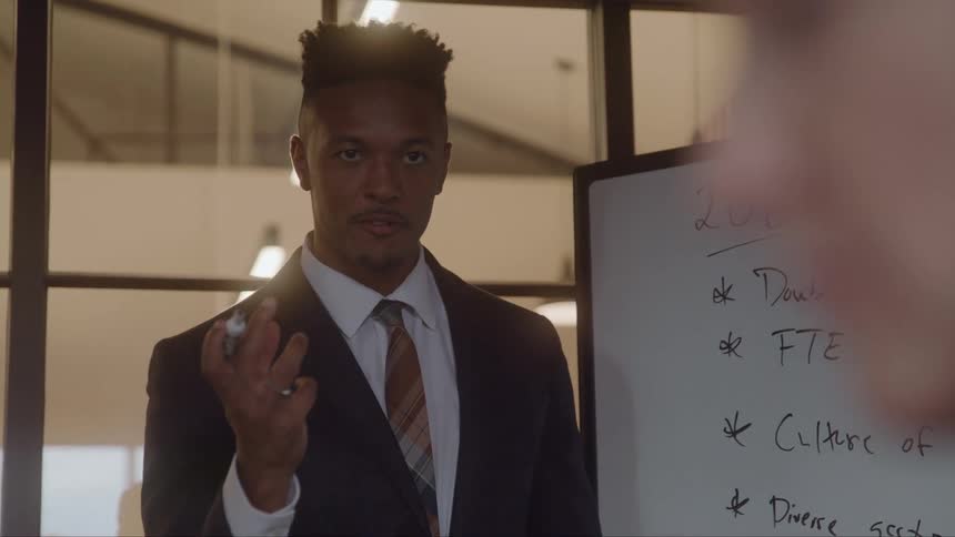 A man standing in an office meeting using a marker and a white board to make a presentation