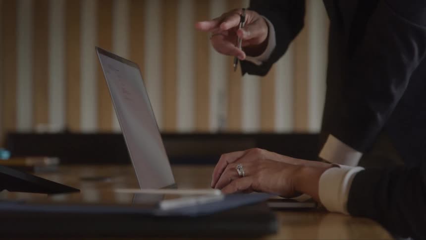 A man is pointing at a laptop as he talks to another man who is typing