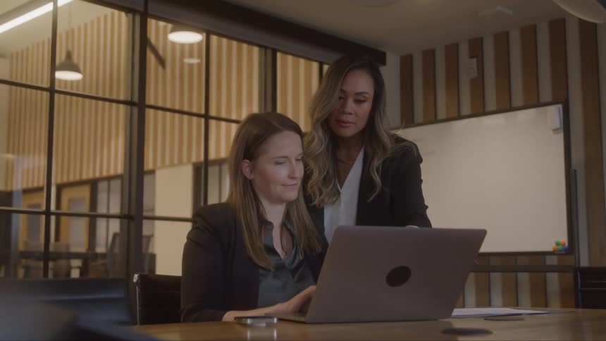 Two women are looking at a computer in an office and pointing and talking