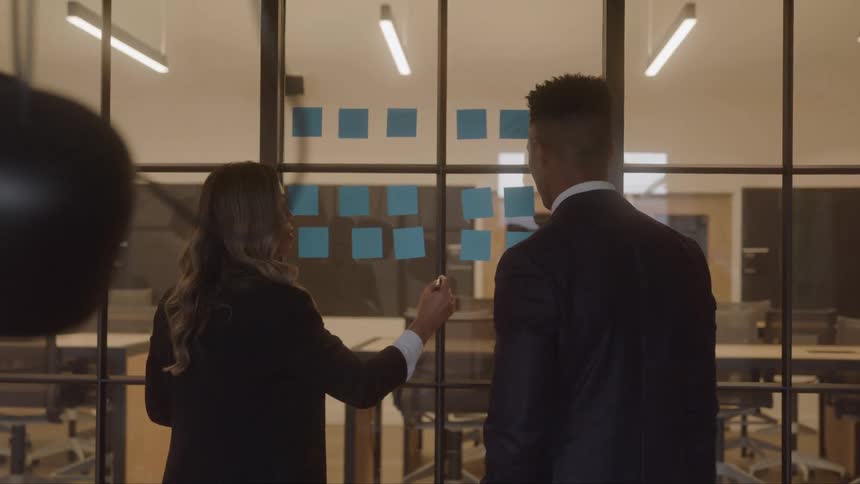 Two people review sticky notes on a glass wall