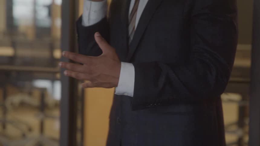 A closeup shot of a man in a business suit talking on his phone while gesturing with his hands in a bright modern office setting