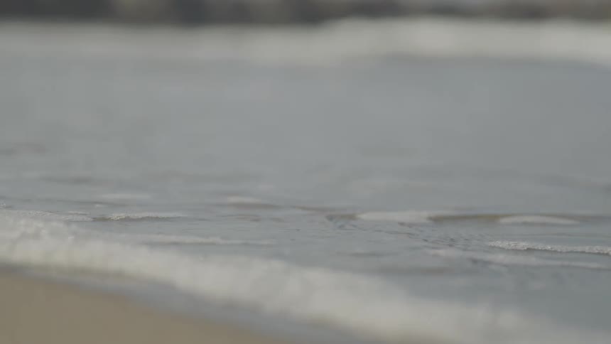 A gentle ocean wave with white foam washes up onto a sandy beach and then slowly recedes back into the sea