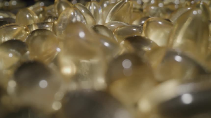 A large pile of translucent yellow oblong capsules with a bright light reflecting off the surface of each one