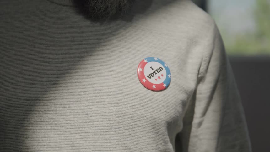 The man puts on an i voted pin on his shirt