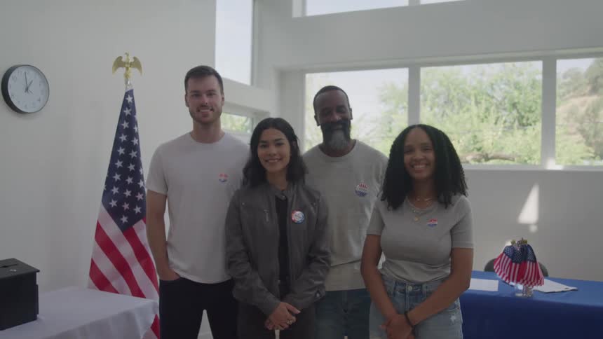 Four young people smiling as they pose for a photo at a polling station