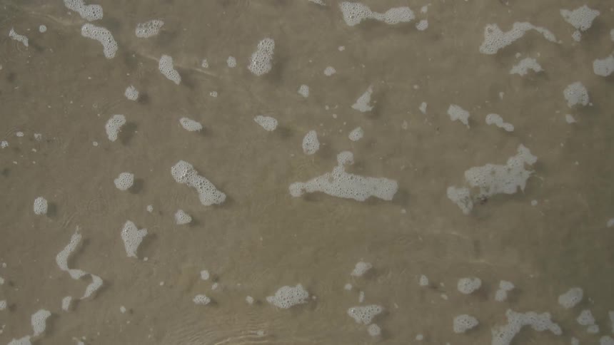 A small ocean wave gently washes upon a sandy beach and then slowly recedes