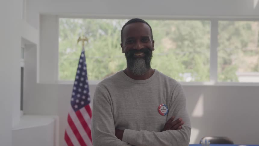Close up of a middle aged black man wearing a voter tag while standing in an office during daytime