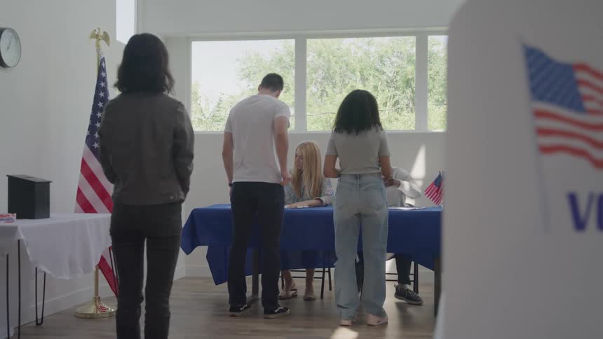 People in line wait for assistance at a polling station with the us flag