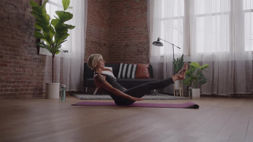 Yoga boat pose in a room with brick wall and plants