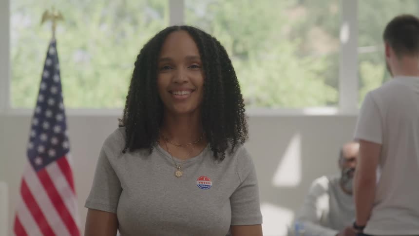 Smiling woman wearing a voting sticker in front of a united states flag