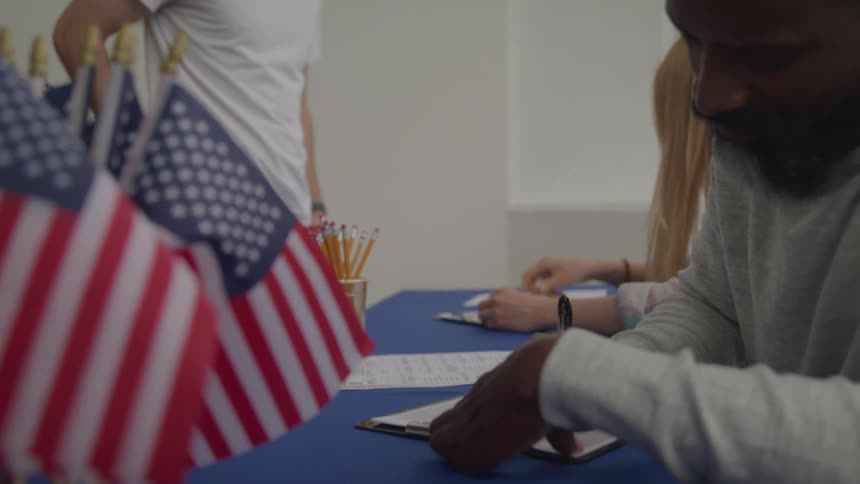An election official hands a ballot to a woman as a line of people waits in the background