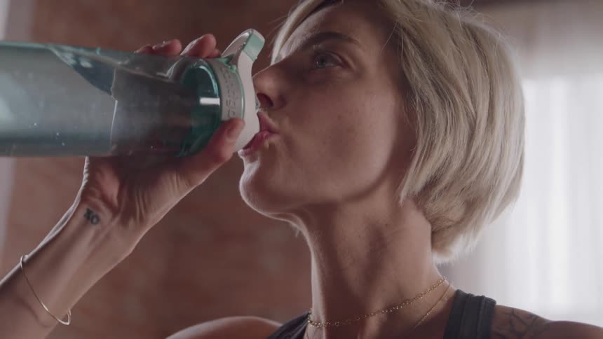 Shorthaired woman drinking water from a transparent bottle with green lid