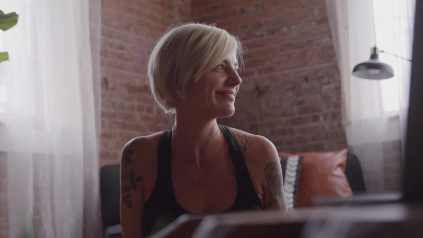 The woman smiles while looking at her laptop