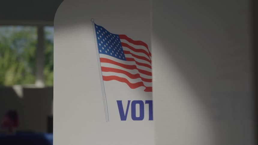 A voting booth with an american flag and the word vote written on its side located in a local polling place
