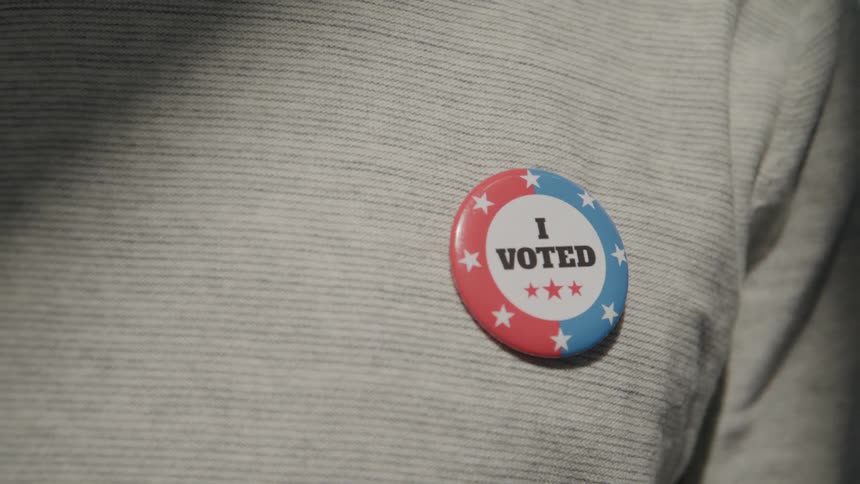 Close up male putting on a i voted button on his shirt