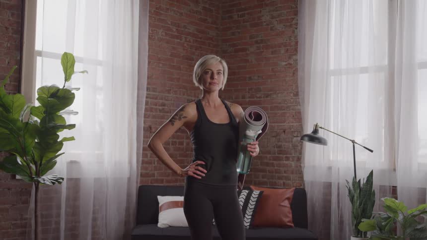 A woman in fitness apparel poses with a yoga mat under her arm