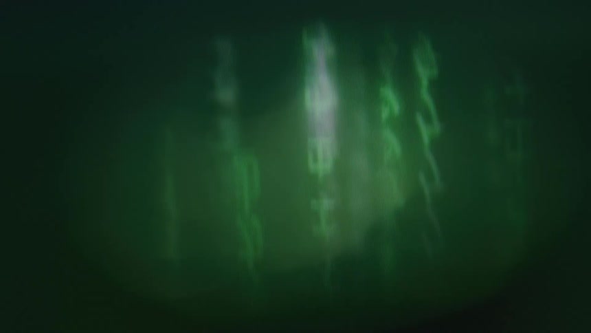 A dark and abstract view shows blurry glowing green and white characters that move vertically across a dark green screen